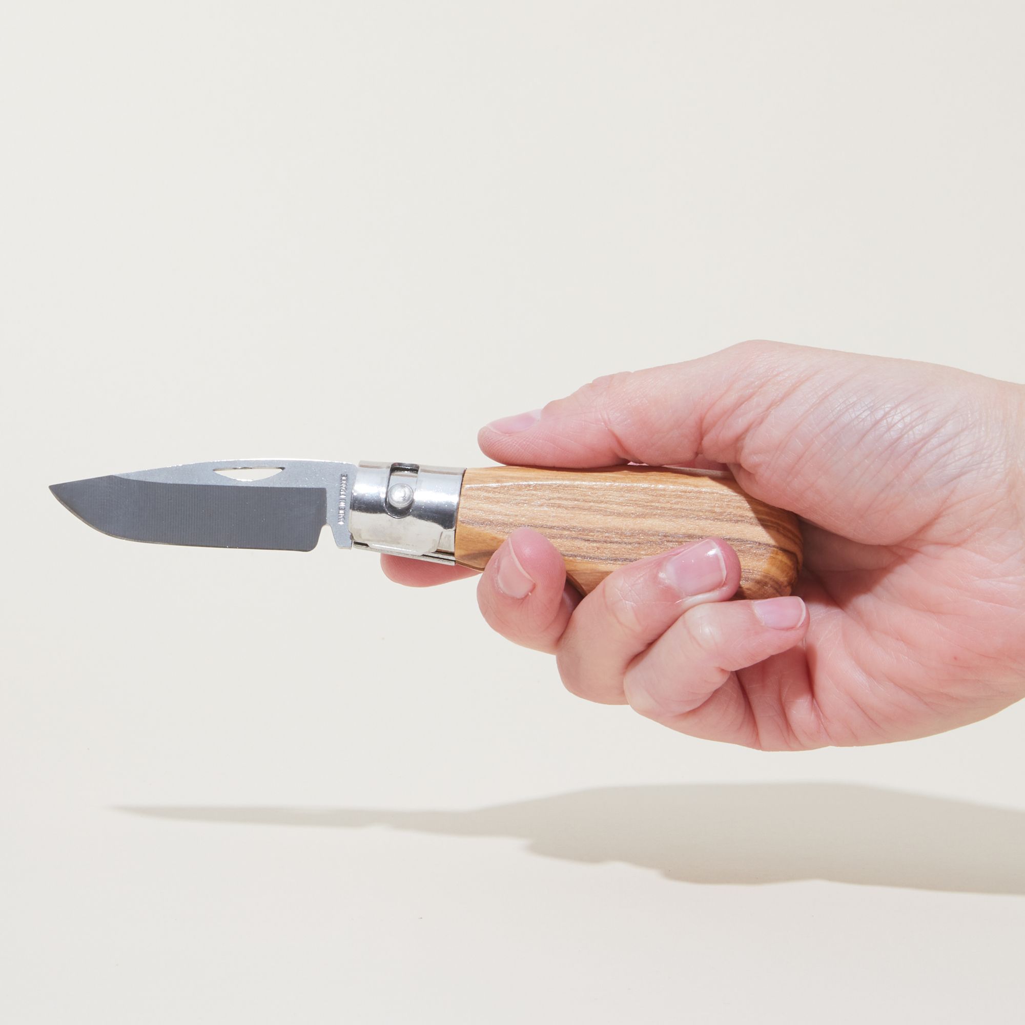 Hand holding an open pocket knife with an olivewood handle
