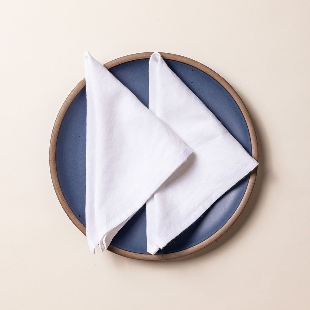 Two white linen napkins folded into triangles on a muted blue ceramic plate.