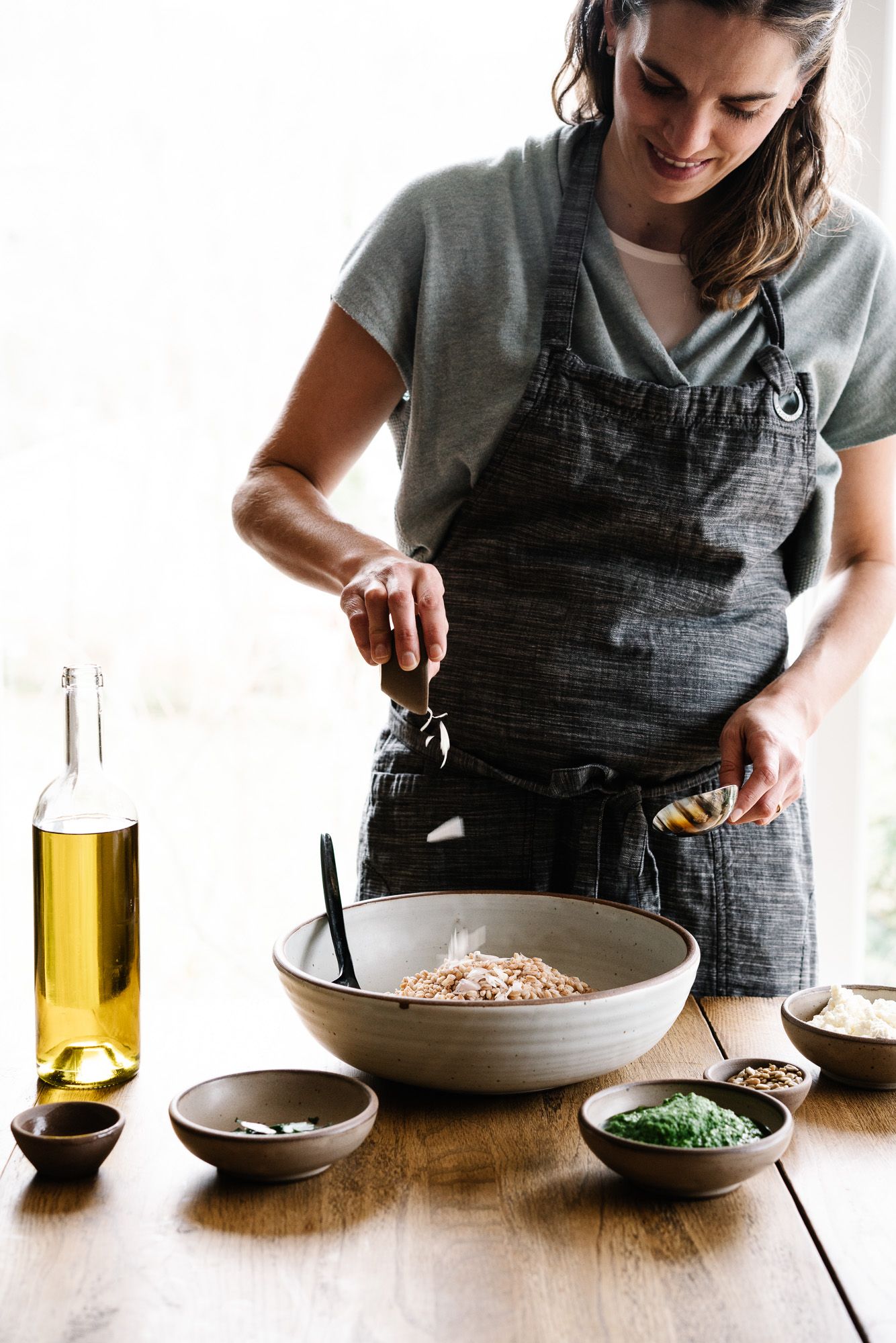 Katie Button is wearing an apron and adding ingredients to a wide bowl