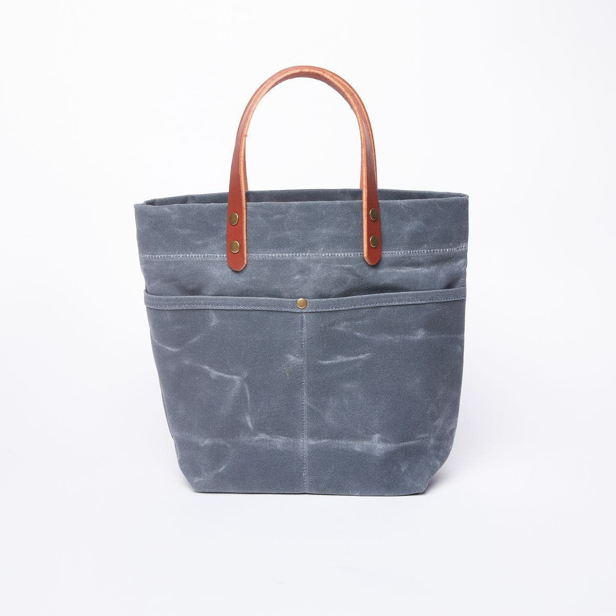 A blue grey waxed canvas bag with two external pockets separated by a rivet and a set of leather handles