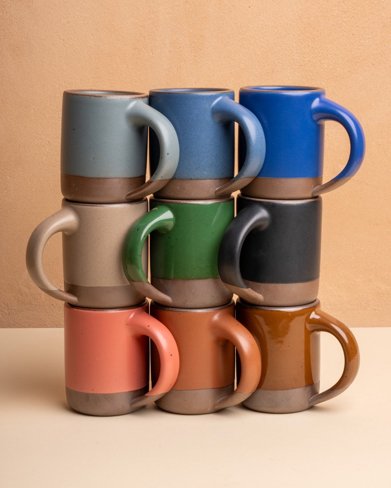 4 ceramic dinner plates, 4 side plates, and 4 shallow dinner bowls in a cool terracotta color with iron speckles and unglazed rims are stacked all together on a table with silverware.