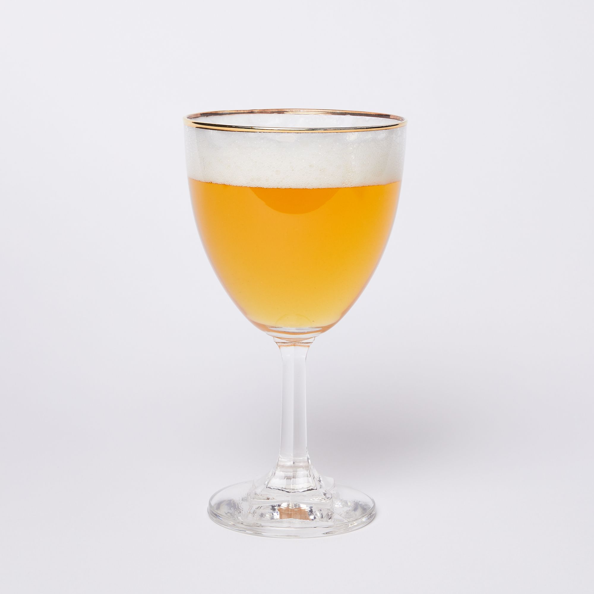A stemmed clear beer glass with a gold rim full of beer with a thick layer of foam