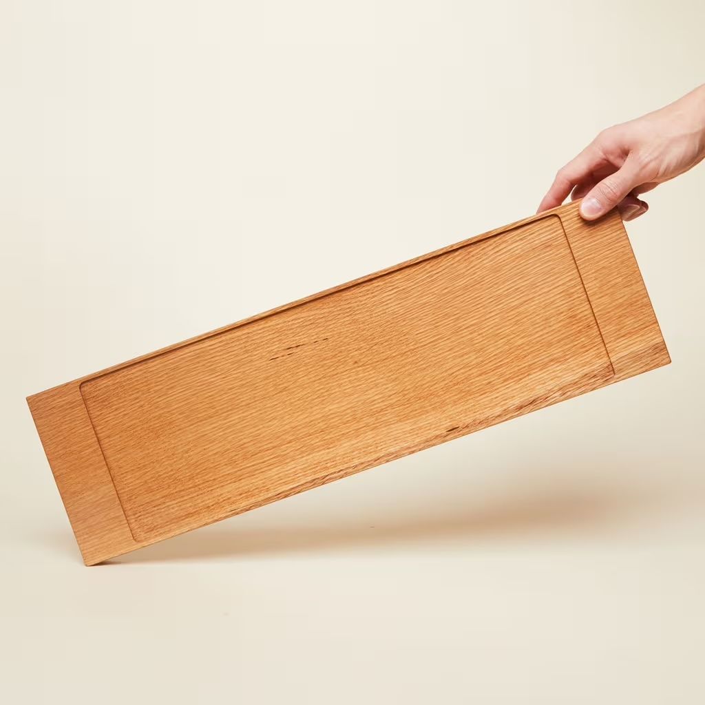 A hand holds up a long rectangular wooden charcuterie board