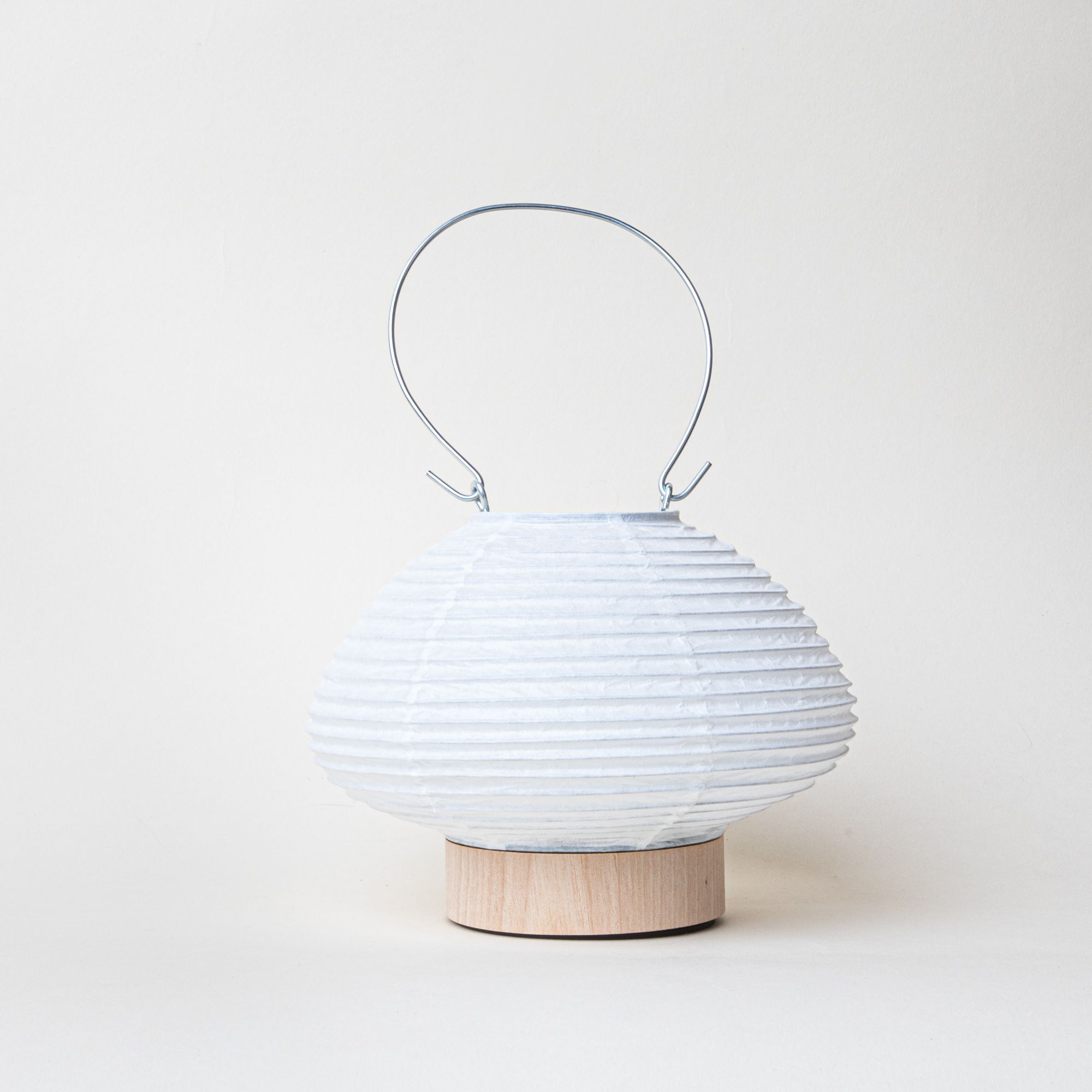 White paper lantern in a short horizontal oval shape with a wood base and a thin metal handle