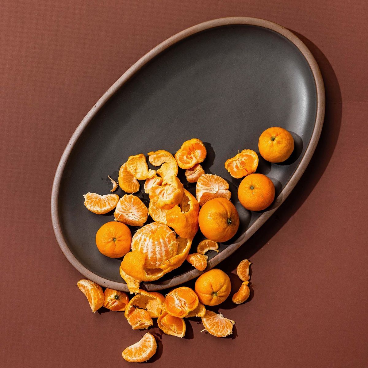 A large oval ceramic platter in a cool, medium grey color featuring iron speckles and an unglazed rim - styled with citrus fruits on a charcoal background