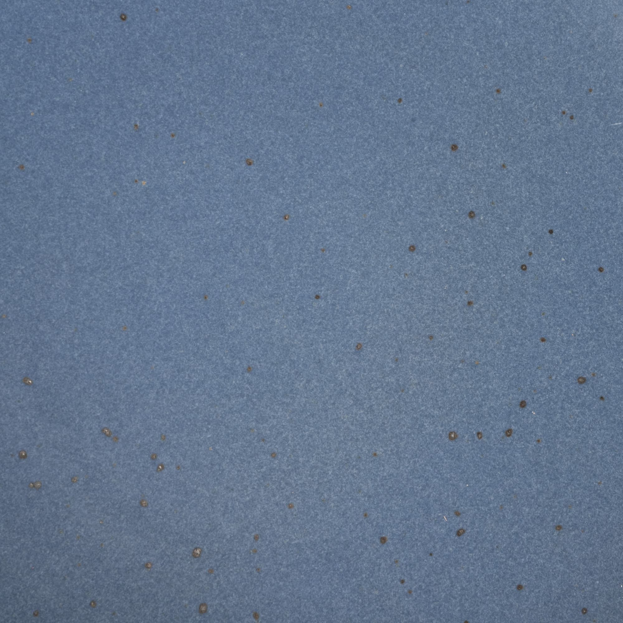 A closeup of a ceramic plate in a cool medium blue color with iron speckles throughout