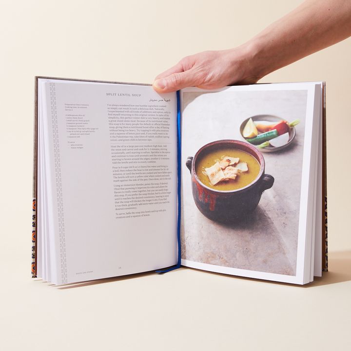 Hand holding a book open with a photo of lentil soup on the right with the corresponding recipe on the left side.