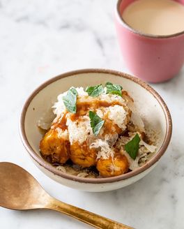Caramelized plantains in an off-white ceramic bowl with a pink cup of chai and brass spoon