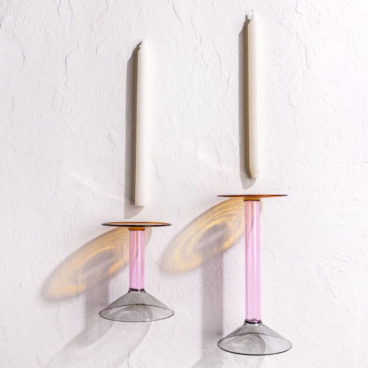 Two modern angular glass candle holder in yellow, pink, and grey colorblocks with cream taper candles