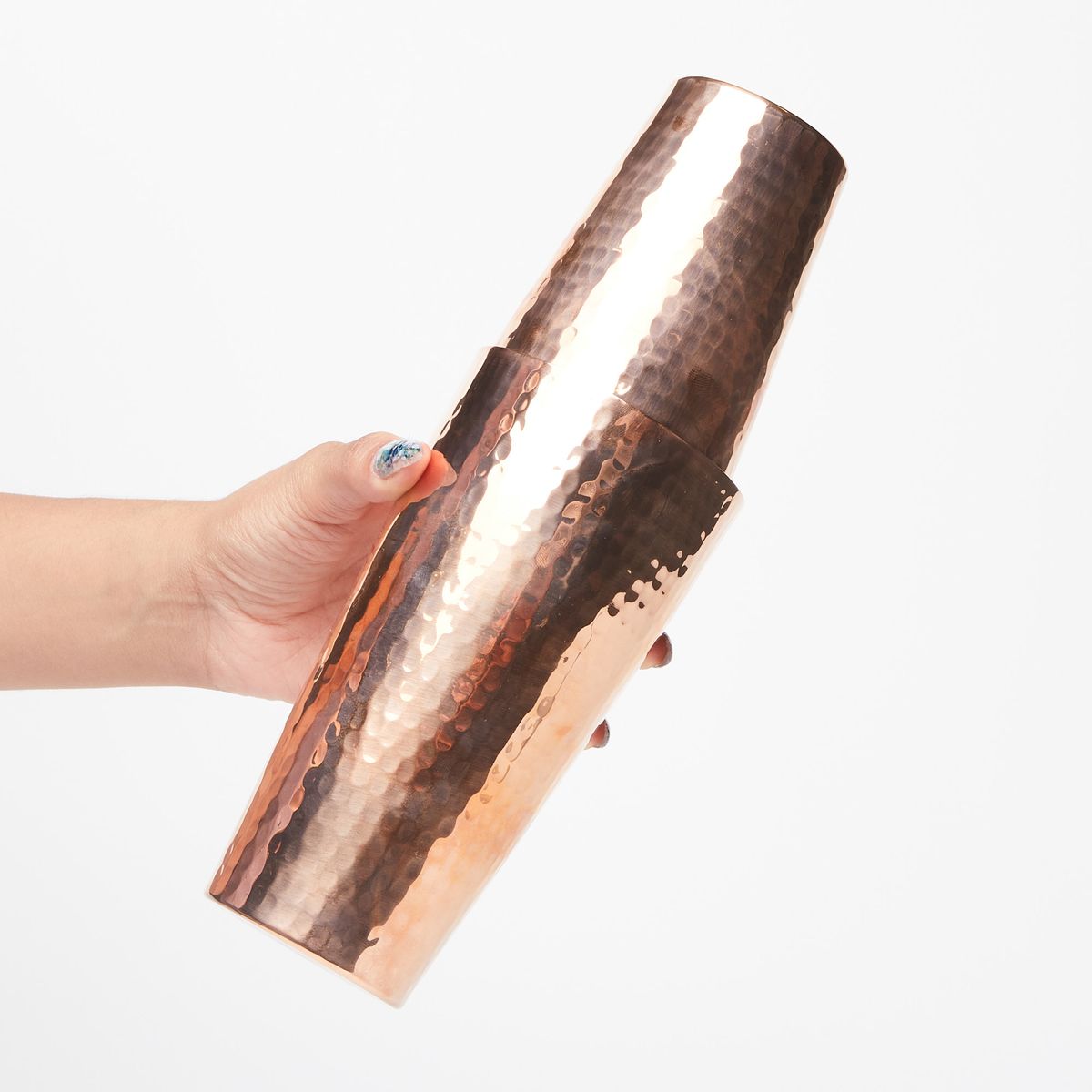 Hand holding a set of two copper cups to make a Boston shaker, with the smaller cup upside down inside the larger cup