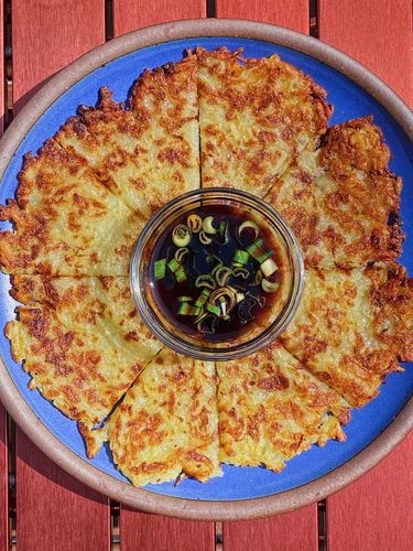 A crispy potato pancake on a large dinner plate in a blue color with a dipping sauce in the middle.