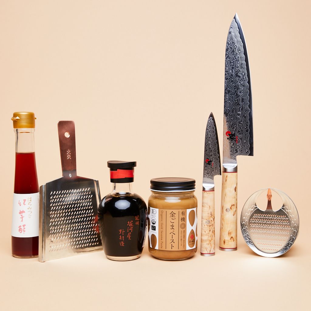 A collection of kitchen tools and bottles of dark-colored liquids that contain vinegar, soy sauce and sesame paste