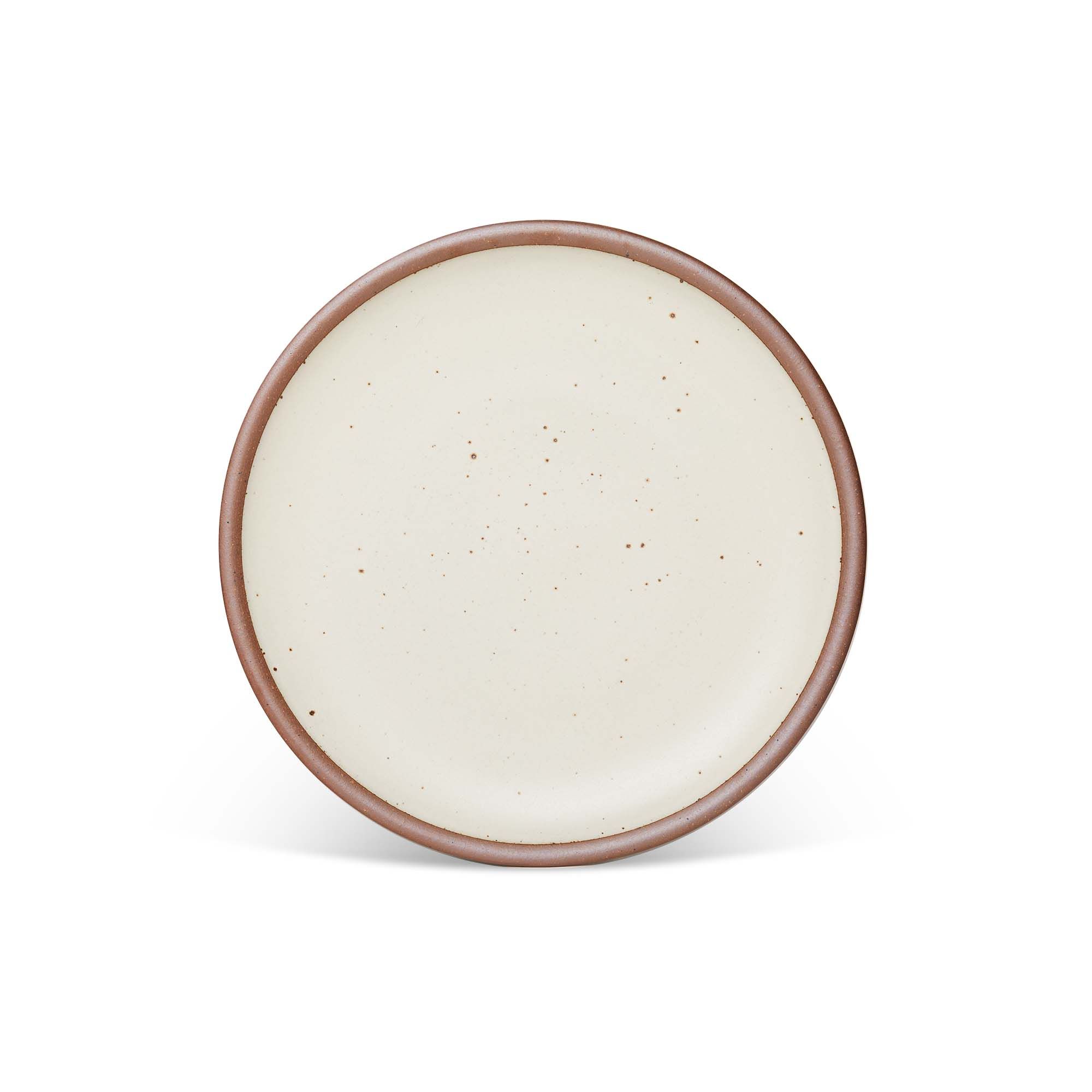 A dinner sized ceramic plate in a warm, tan-toned, off-white color featuring iron speckles and an unglazed rim.