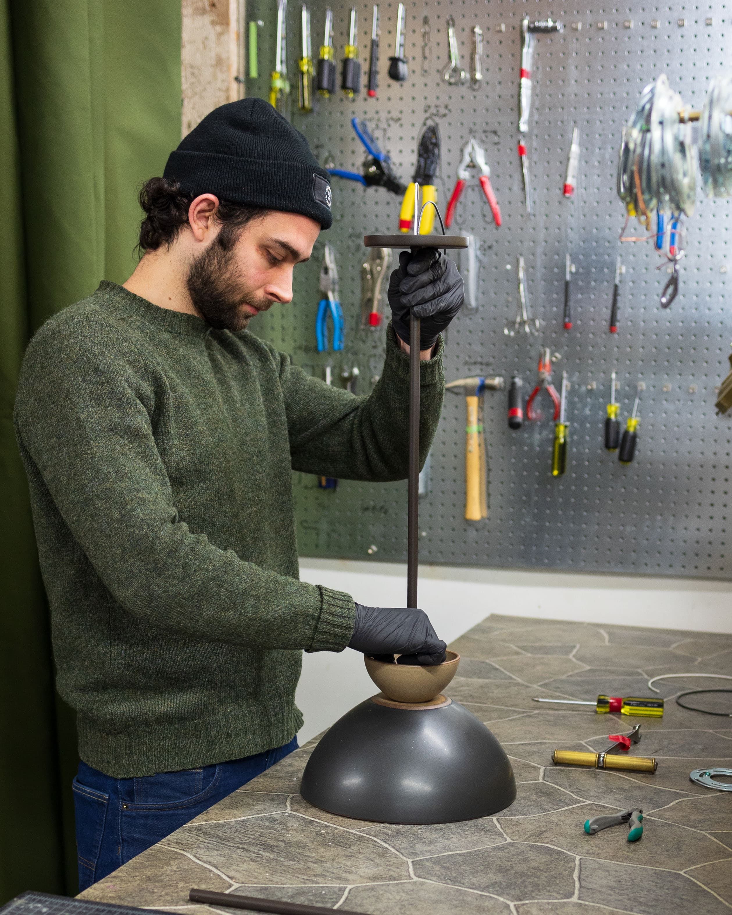 A person assembling a light fixture made from East Fork bowls in front of a wall of handtools