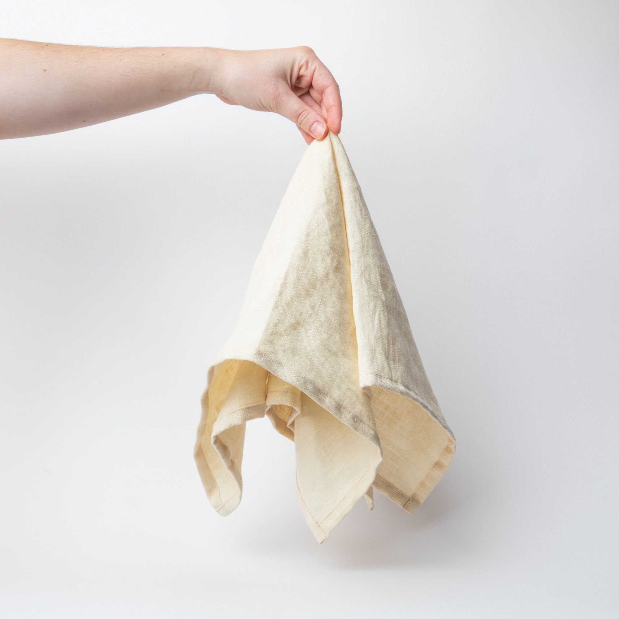 Hand holding a linen napkin in a soft butter yellow from the center 