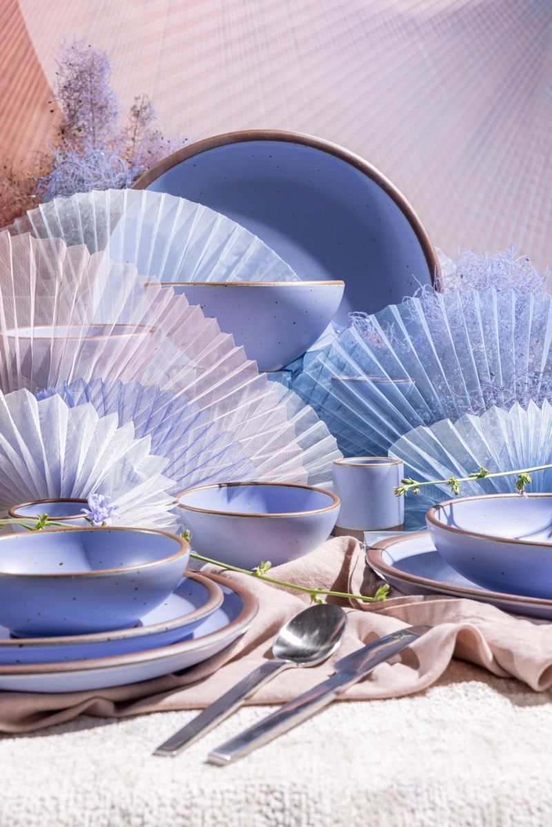 Ceramic bowls in a light periwinkle are artfully styled together on a mirrored surface that reflects fluffy white cloud above.