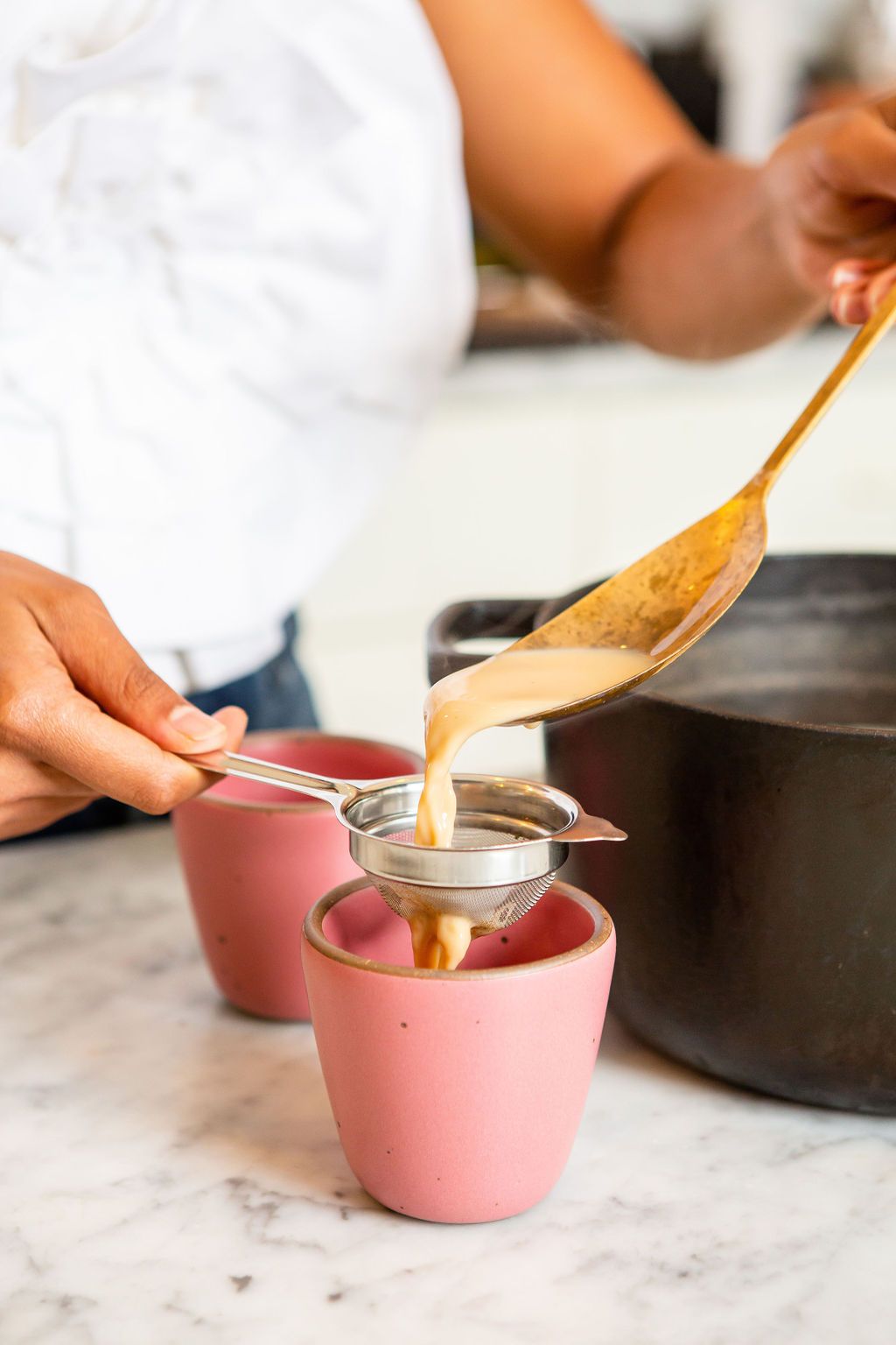 Sana Javeri Kadri, Diaspora Co.’s founder, uses a brass ladle to pour chai from a cast iron pot, through a strainer, and into a hot pink handleless mug made by East Fork.