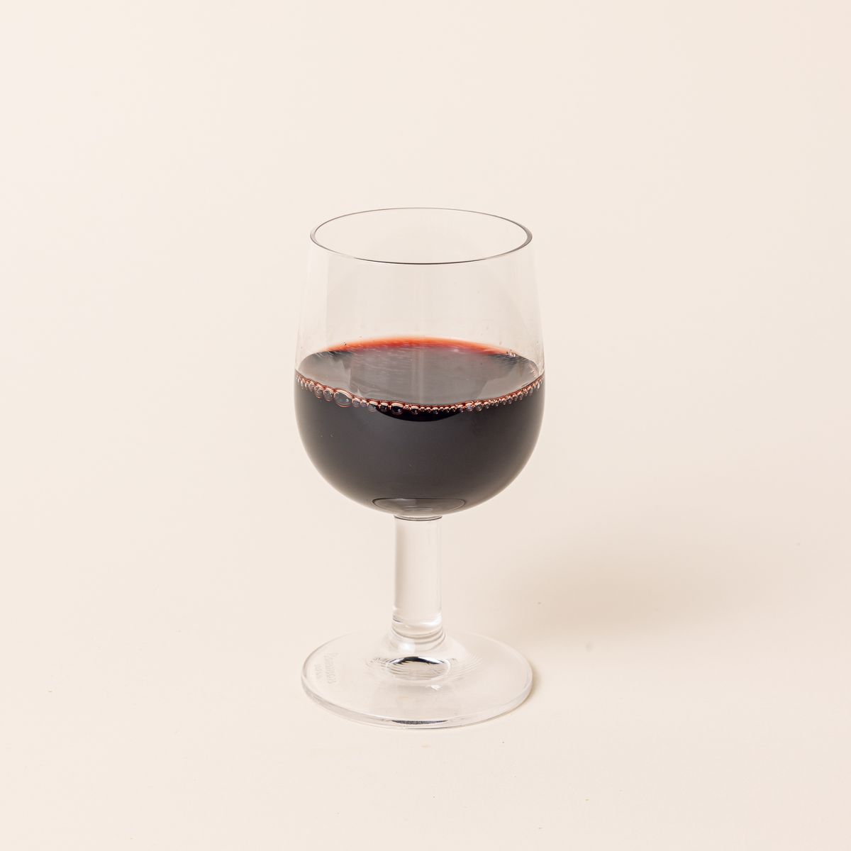 A clear wine glass with a short stem and wide cup, filled with red wine.