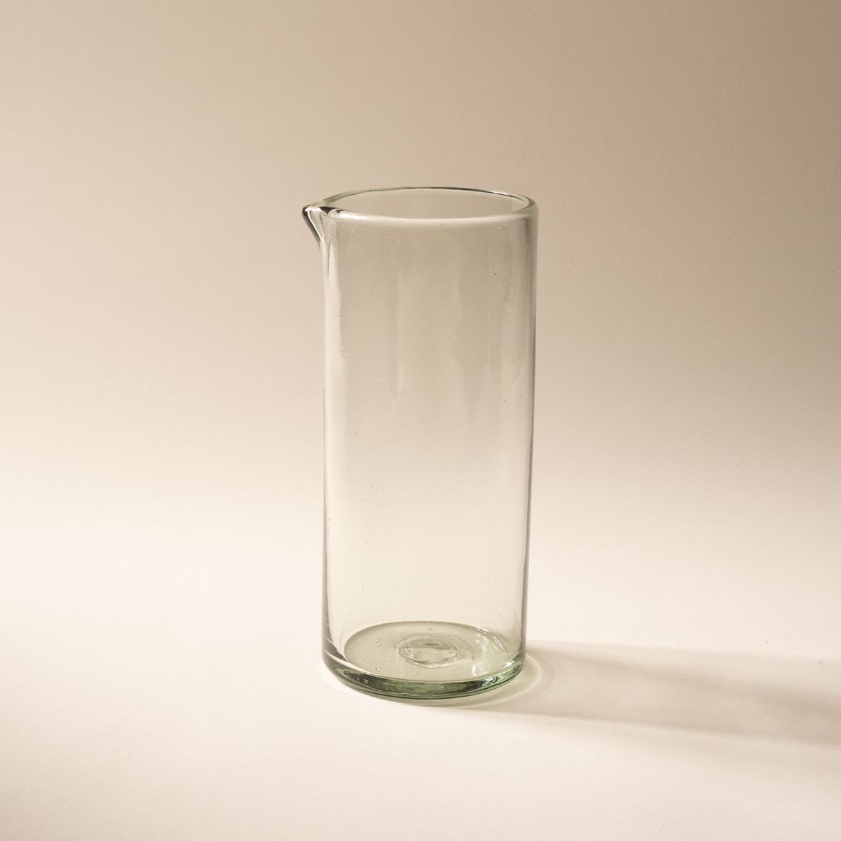 A tall clear glass pitcher with small spout at the top