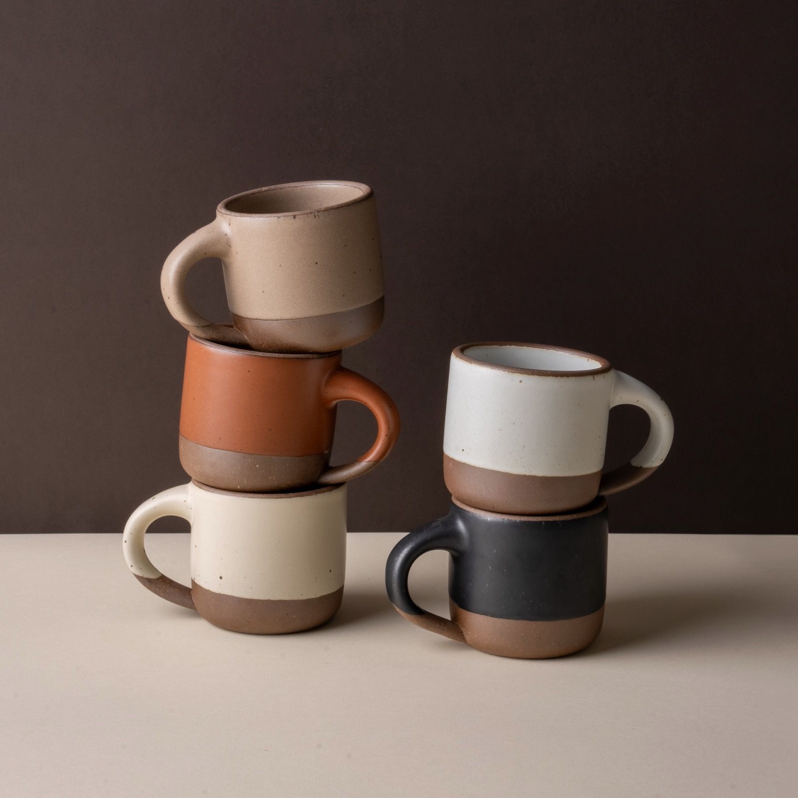 A hand holds out small ceramic mugs on a few fingers and balances 2 small ceramic mugs on the palm of their hand.