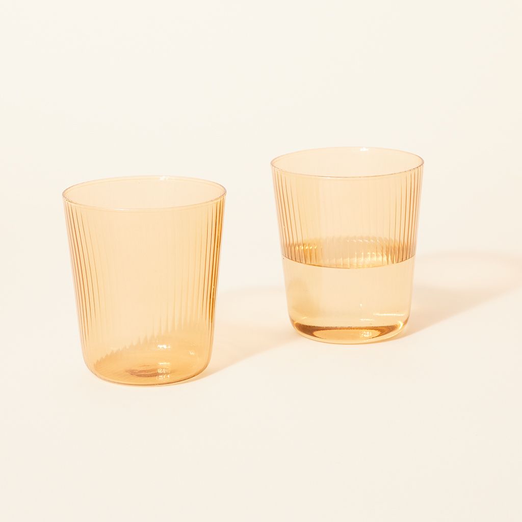 Two pale yellow drinking glasses, one empty and one half full of water