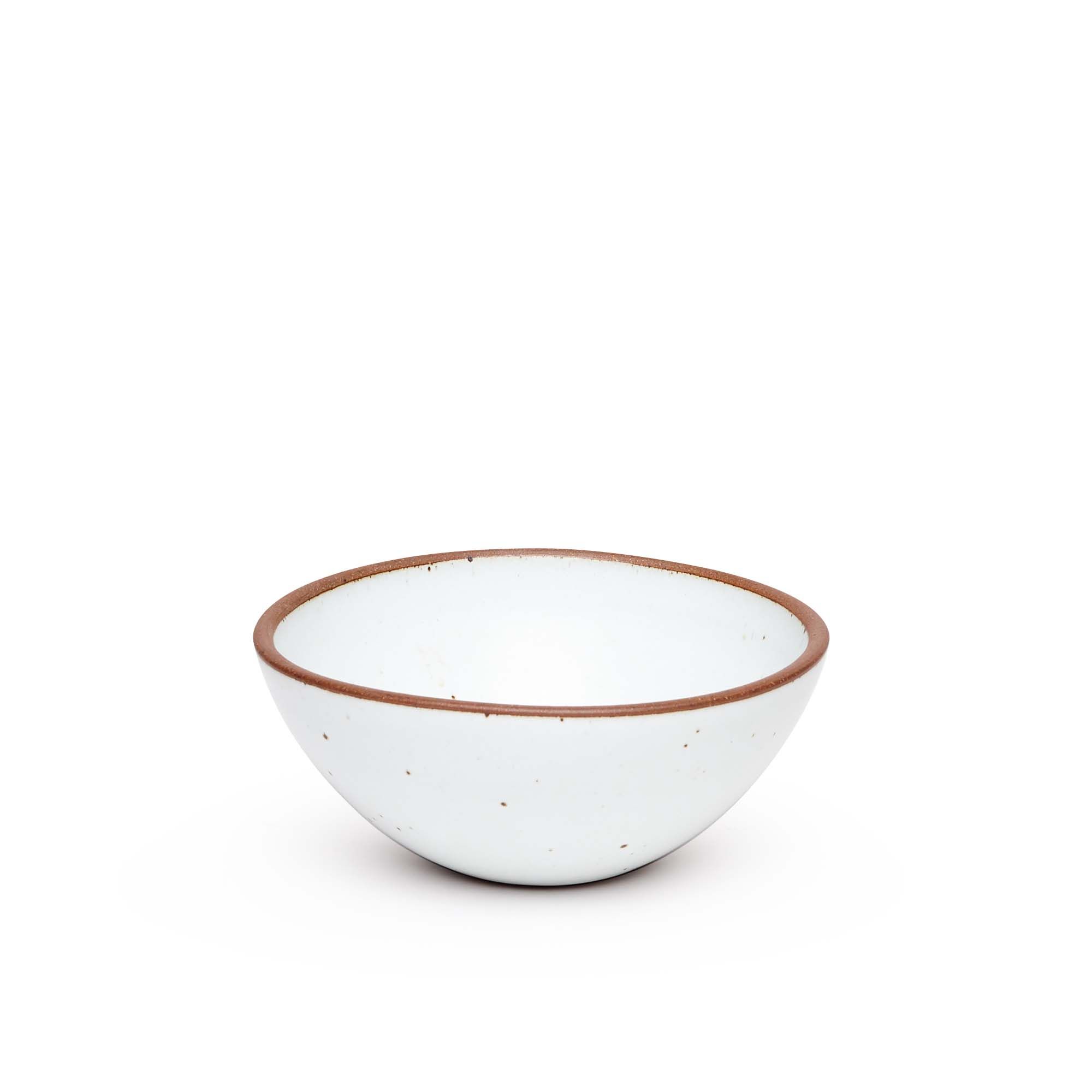 A medium rounded ceramic bowl in a cool white color featuring iron speckles and an unglazed rim