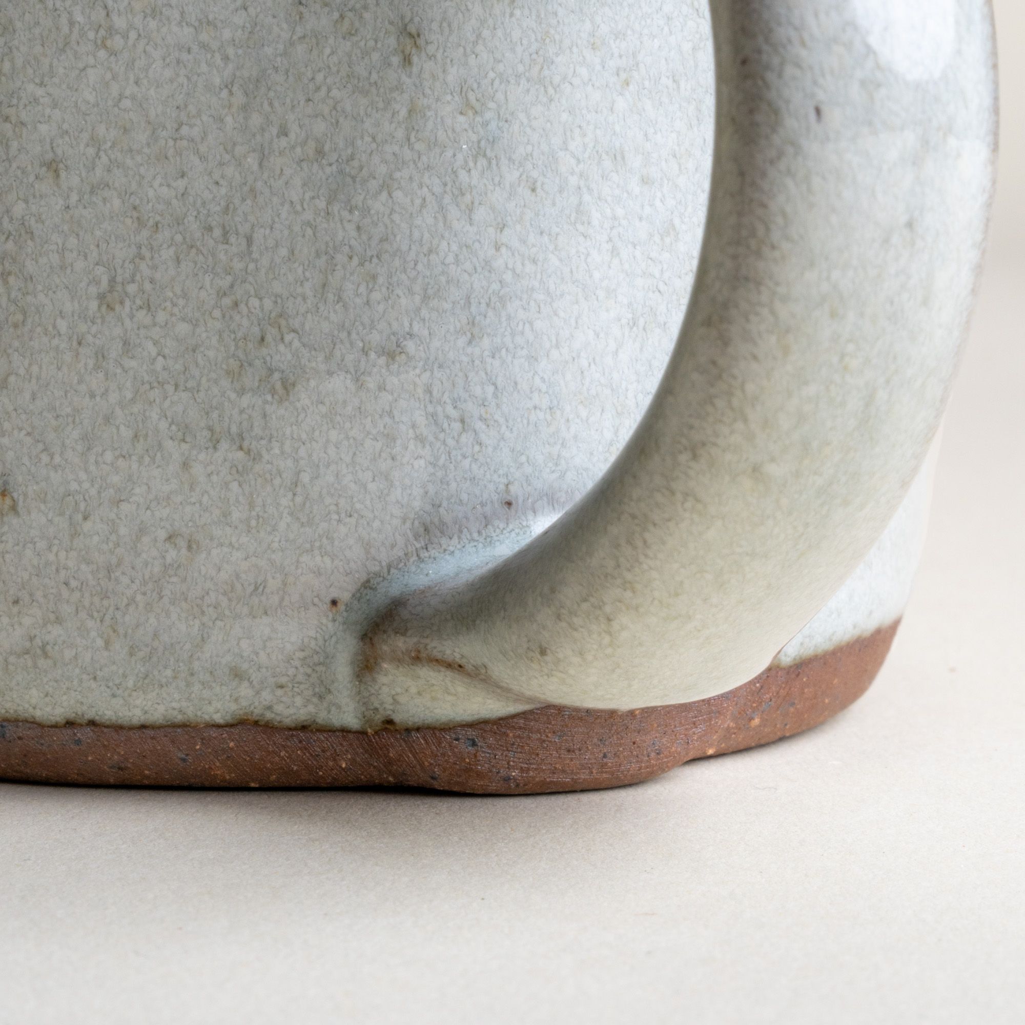 A close up of a handle on a medium sized ceramic mug with handle in a reactive icy white color featuring iron speckles