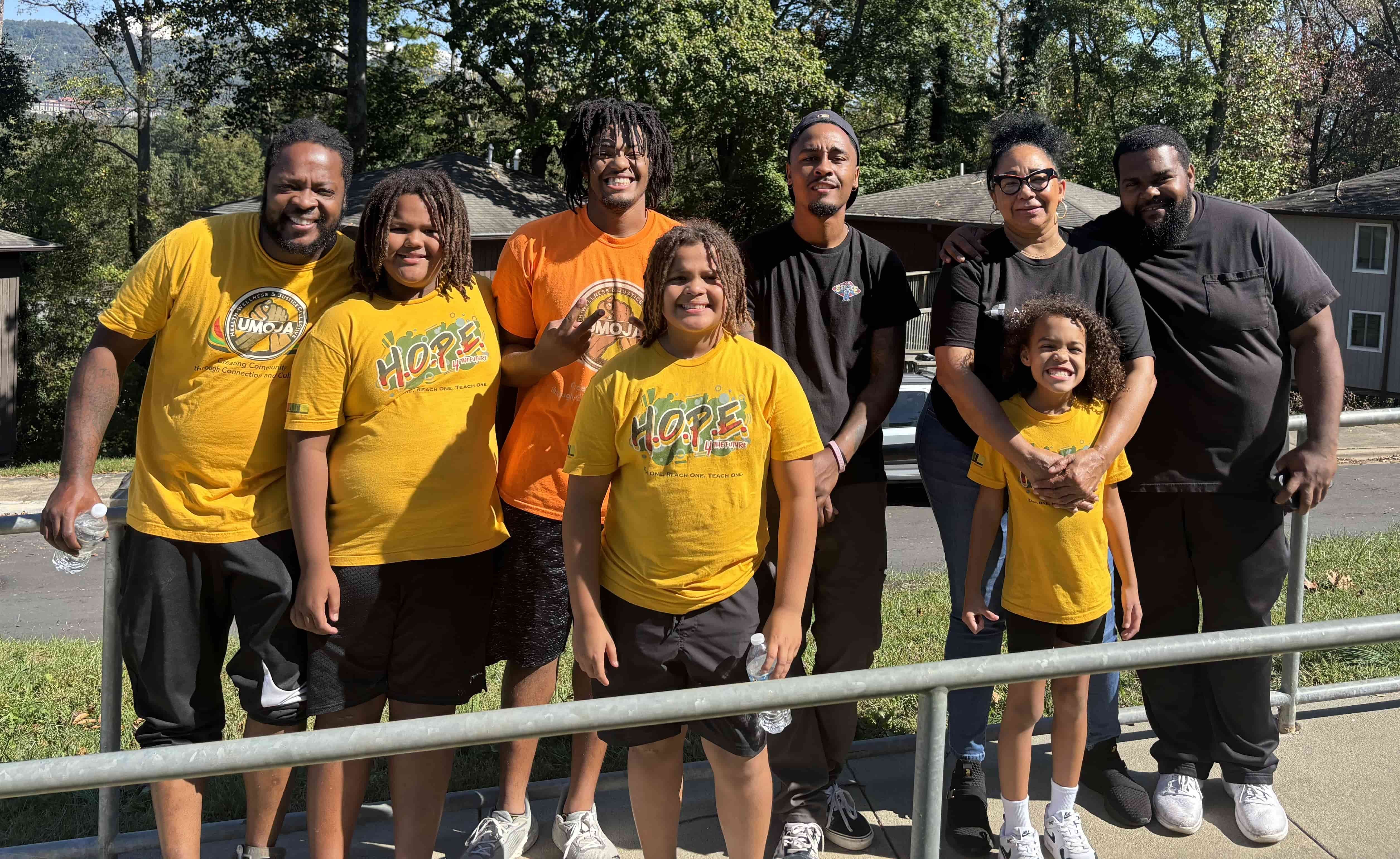 A group of adults and kids are outside and gathered close together smiling at the camera