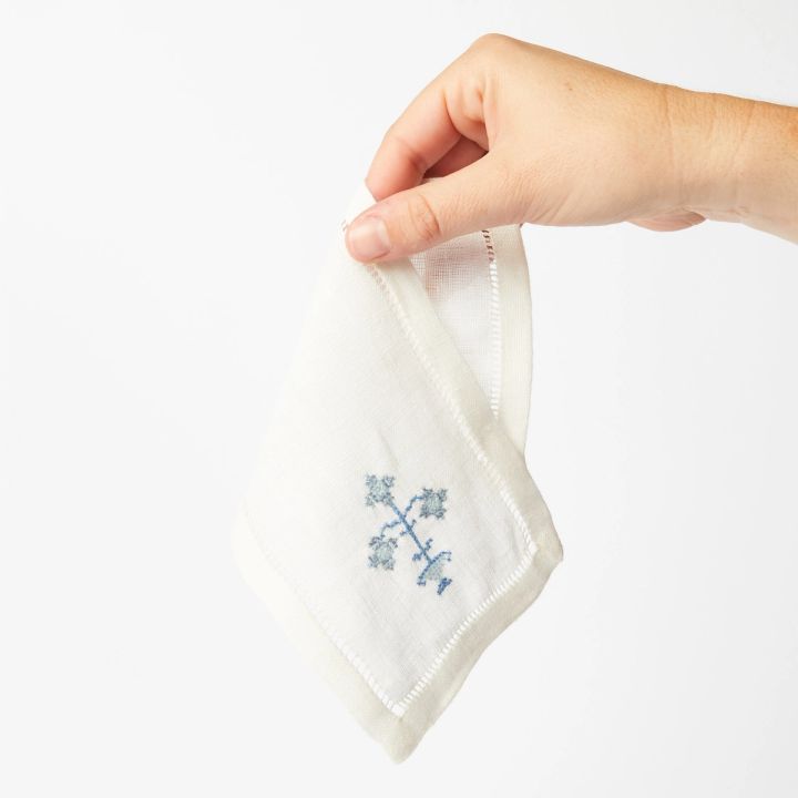 Hand holding cloth napkin with embroidered blue flower