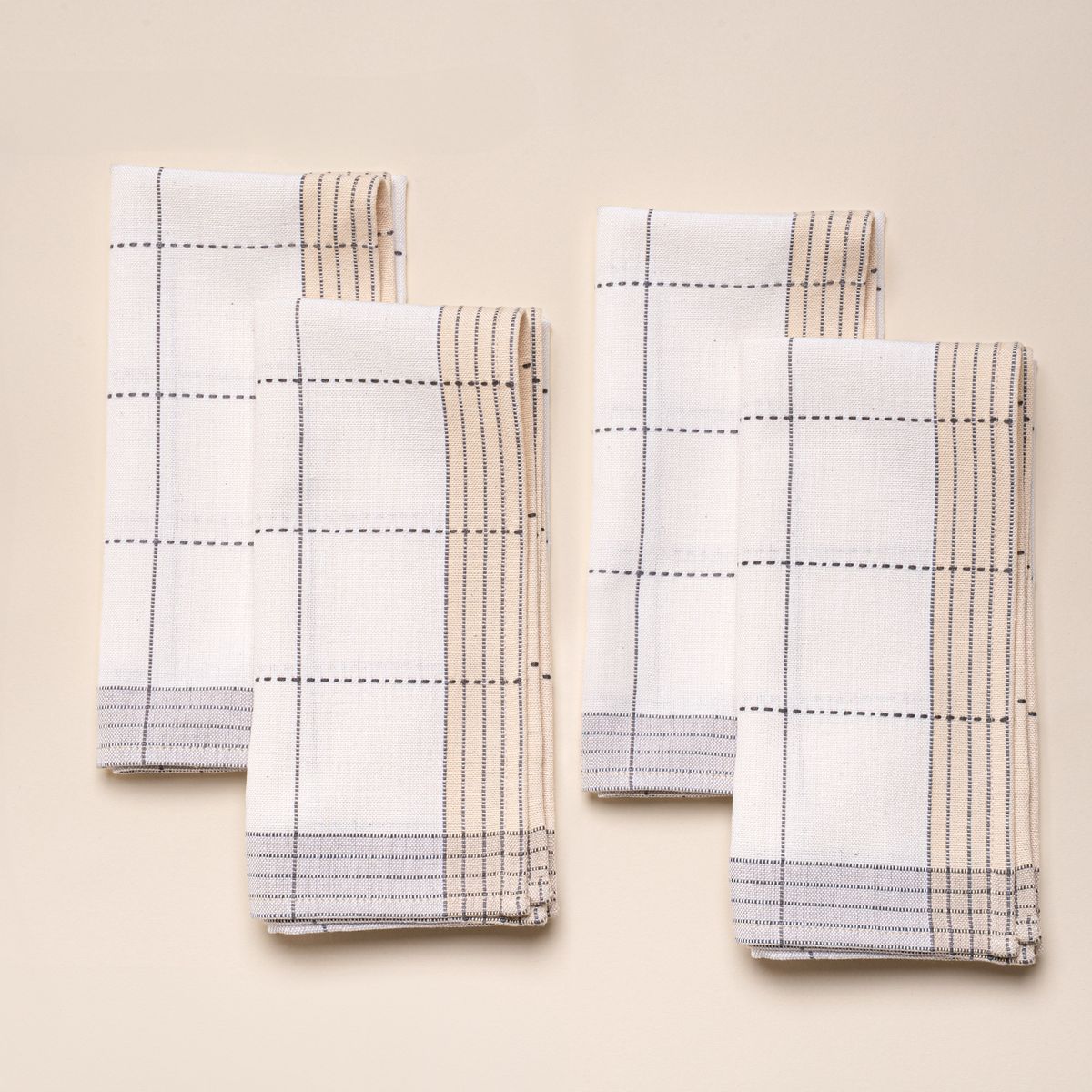 Four folded white colored napkins that are designed with grey gridlines with light grey and natural striped edging.