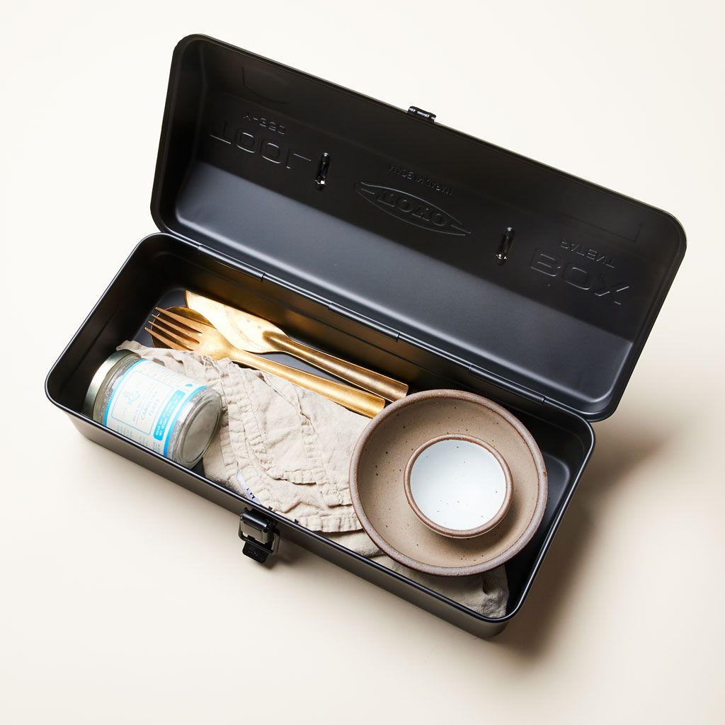 Overhead view of open metal box that contains eating utensils, bowls, a napkin and a jar of salt