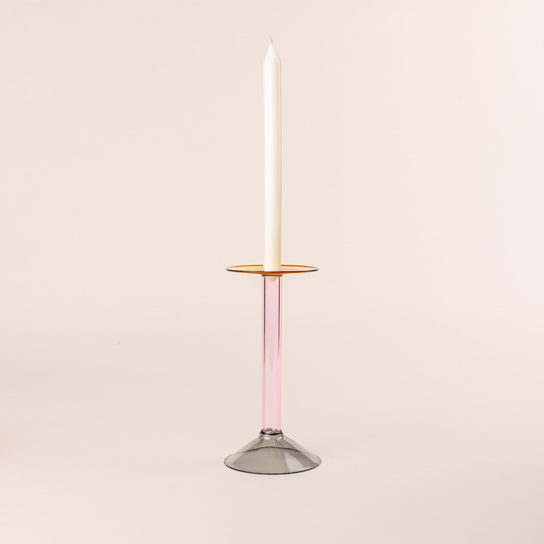 A tall modern angular glass candle holder in yellow, pink, and grey colorblocks with a cream taper candle