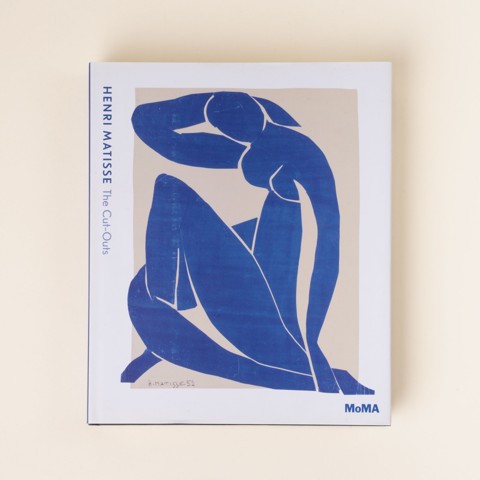 The cover of Henri Matisse: The Cut-Outs from MoMA, featuring Matisse’s blue cut-out artwork of a seated figure on a beige background.