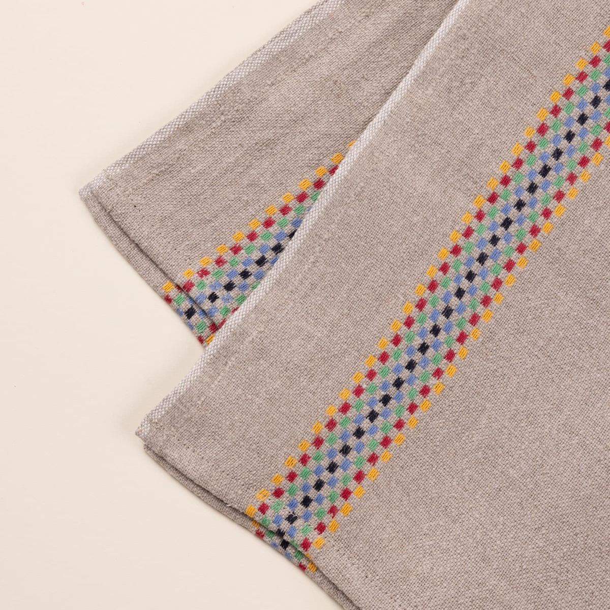 A closeup of a folded linen towel in a beige color with a multicolor checkerboard stripe down the side