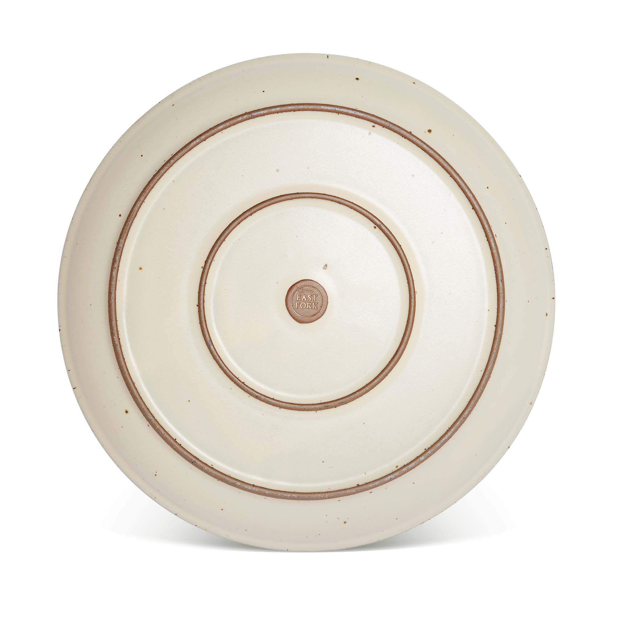 Bottom of a large ceramic platter in a warm, tan-toned, off-white color featuring iron speckles and an unglazed rim