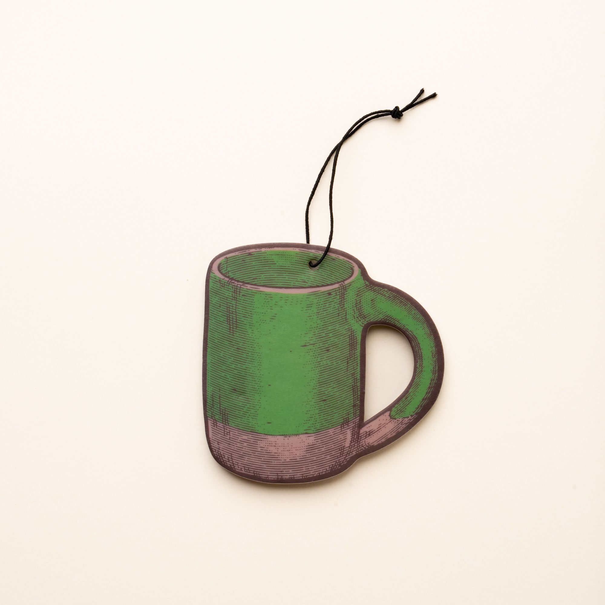 Illustrated mug-shaped air freshener in a green color with a black hanging string against a light cream background.