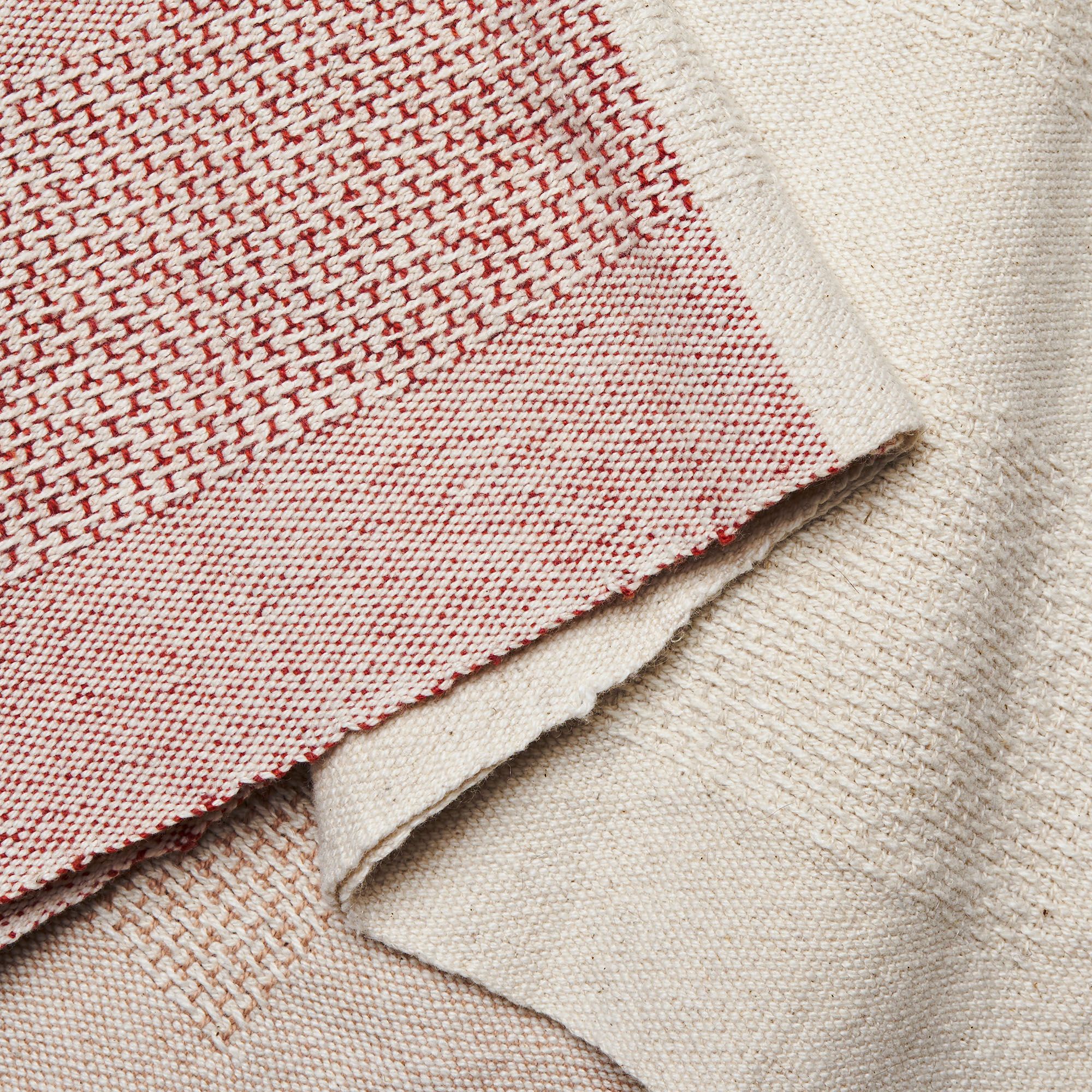 A close up shot of a part-earthy red, part-natural fiber tea towel, showing how the red and white fibers are woven together