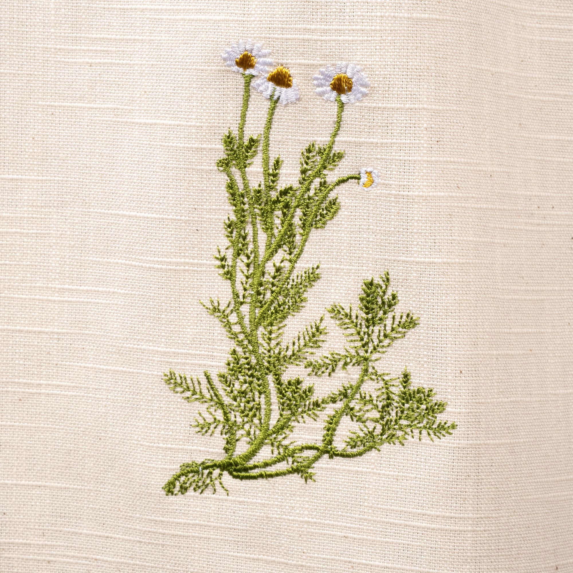 A close up of a white and green embroidered flower on a canvas apron.