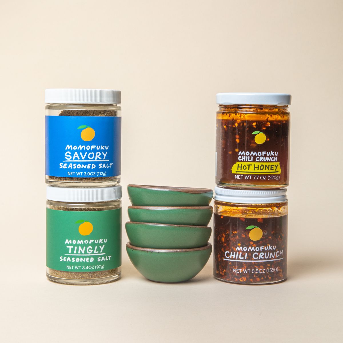 4 stacked little ceramic bowls in a cool green color surrounded by 4 jars of Momofuku seasoned salts and chili crunch.