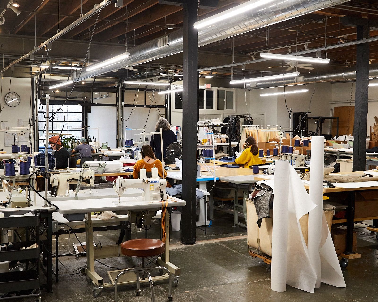 Inside a large sewing studio with several desks and sewing machines set up with people working at them.