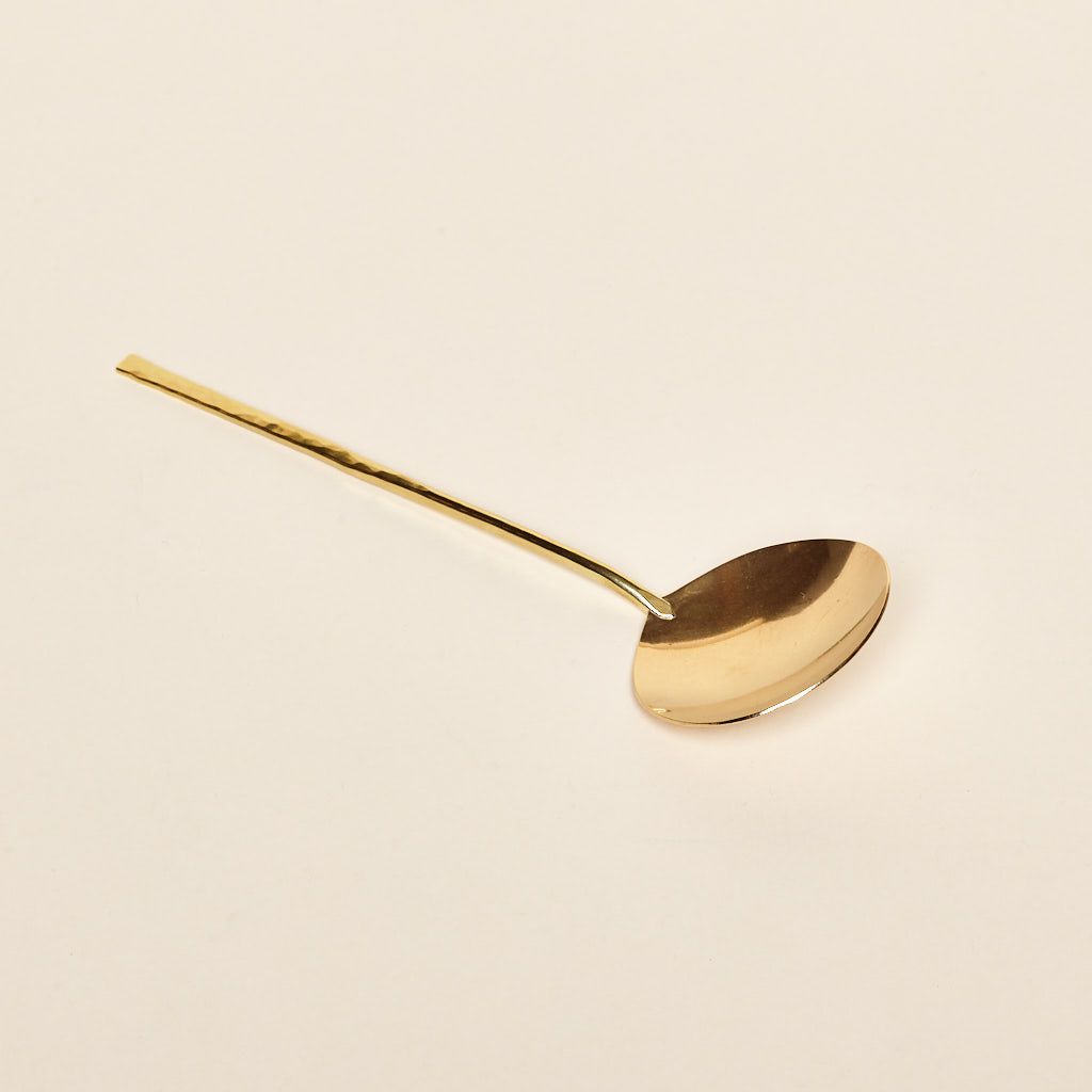 Brass serving spoon that is shiny and gold in color