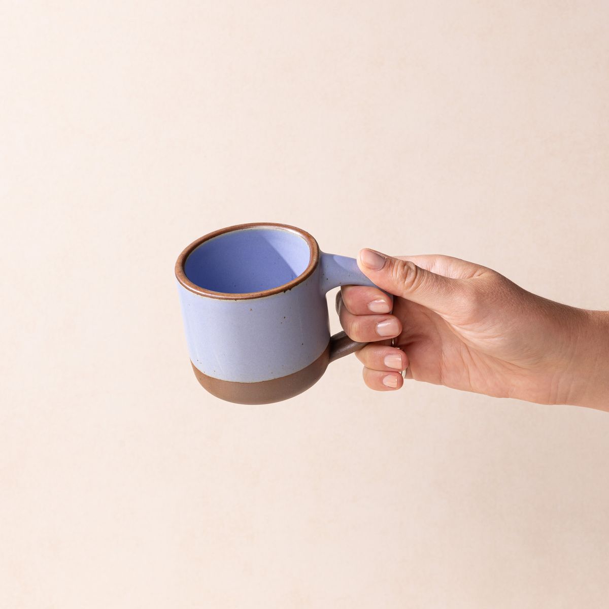 A hand holds a small sized ceramic mug with handle in a periwinkle featuring an unglazed rim