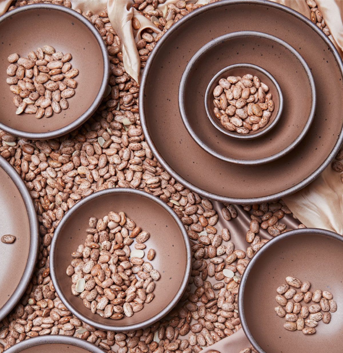 An overhead view of pots in various sizes in a pinto bean color are filled with dried beans.