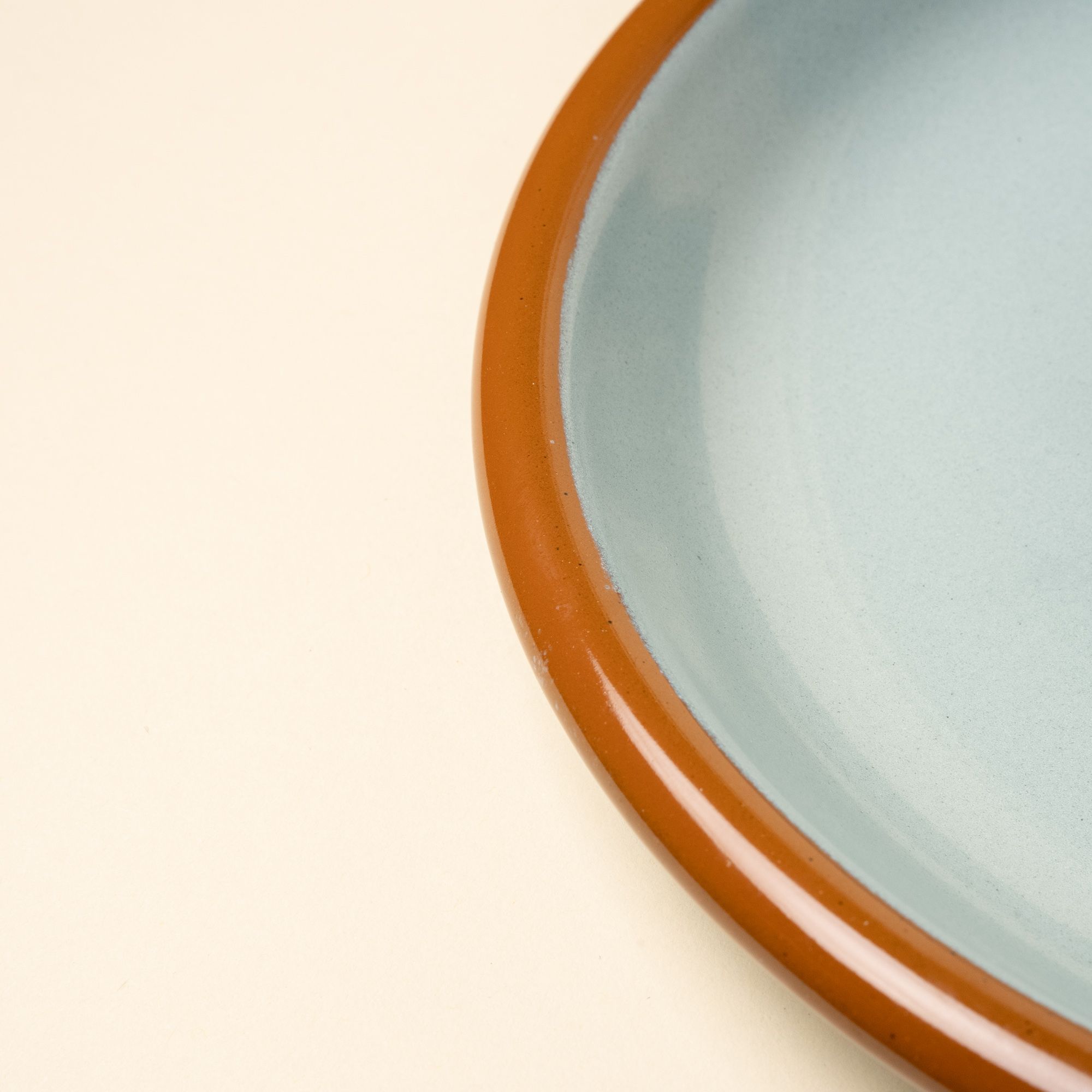 A closeup of the rim of a robin's egg blue enamel plate with warm brown rim.