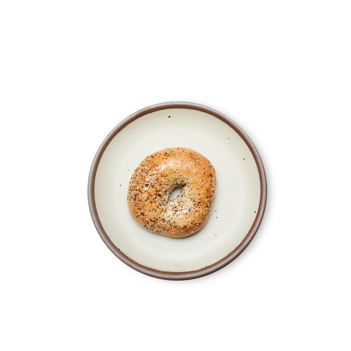 A bagel on a medium sized ceramic plate in a warm, tan-toned, off-whitecolor featuring iron speckles and an unglazed rim.