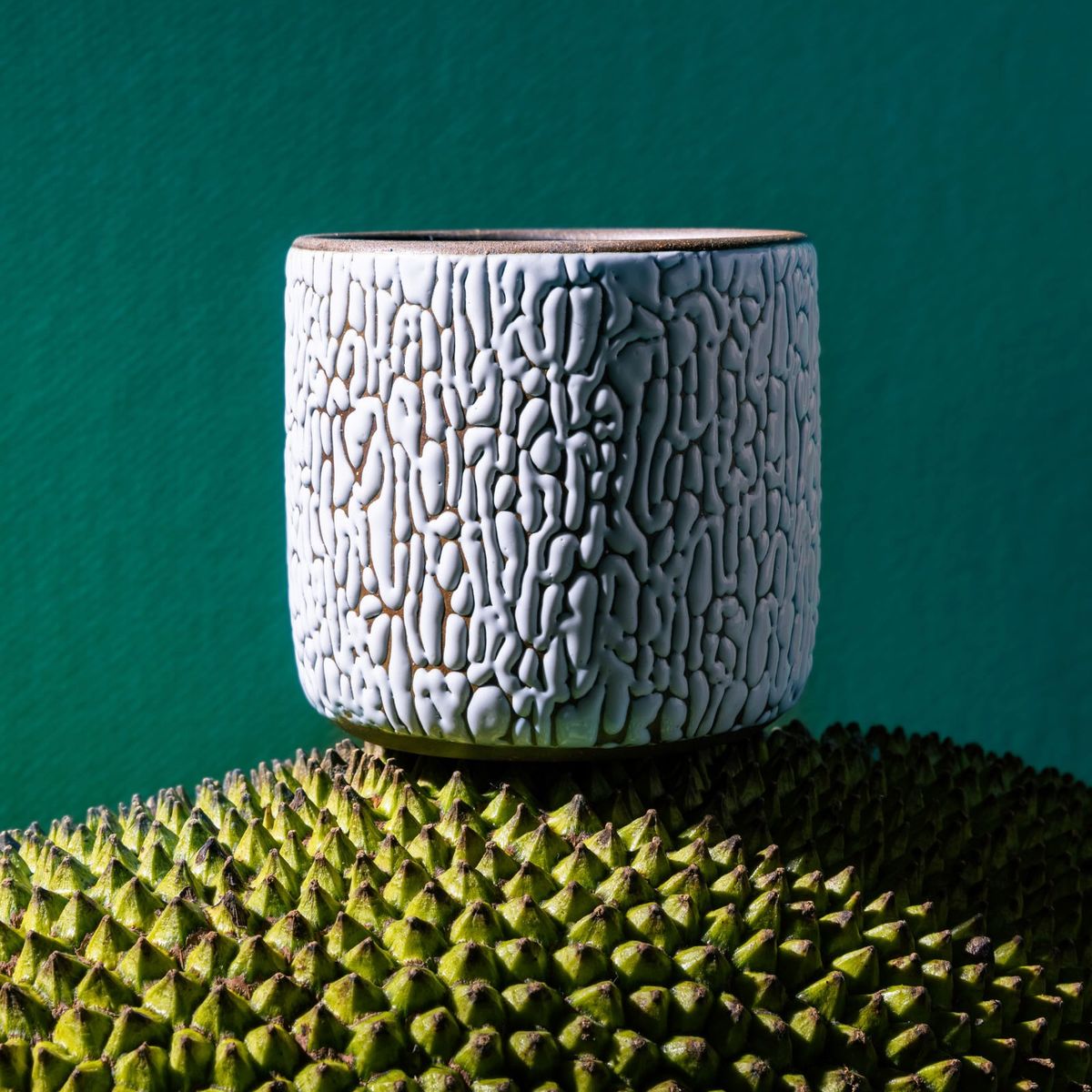 A white ceramic vessel with cracked texture sits on top of a green textured sphere with a dark teal background