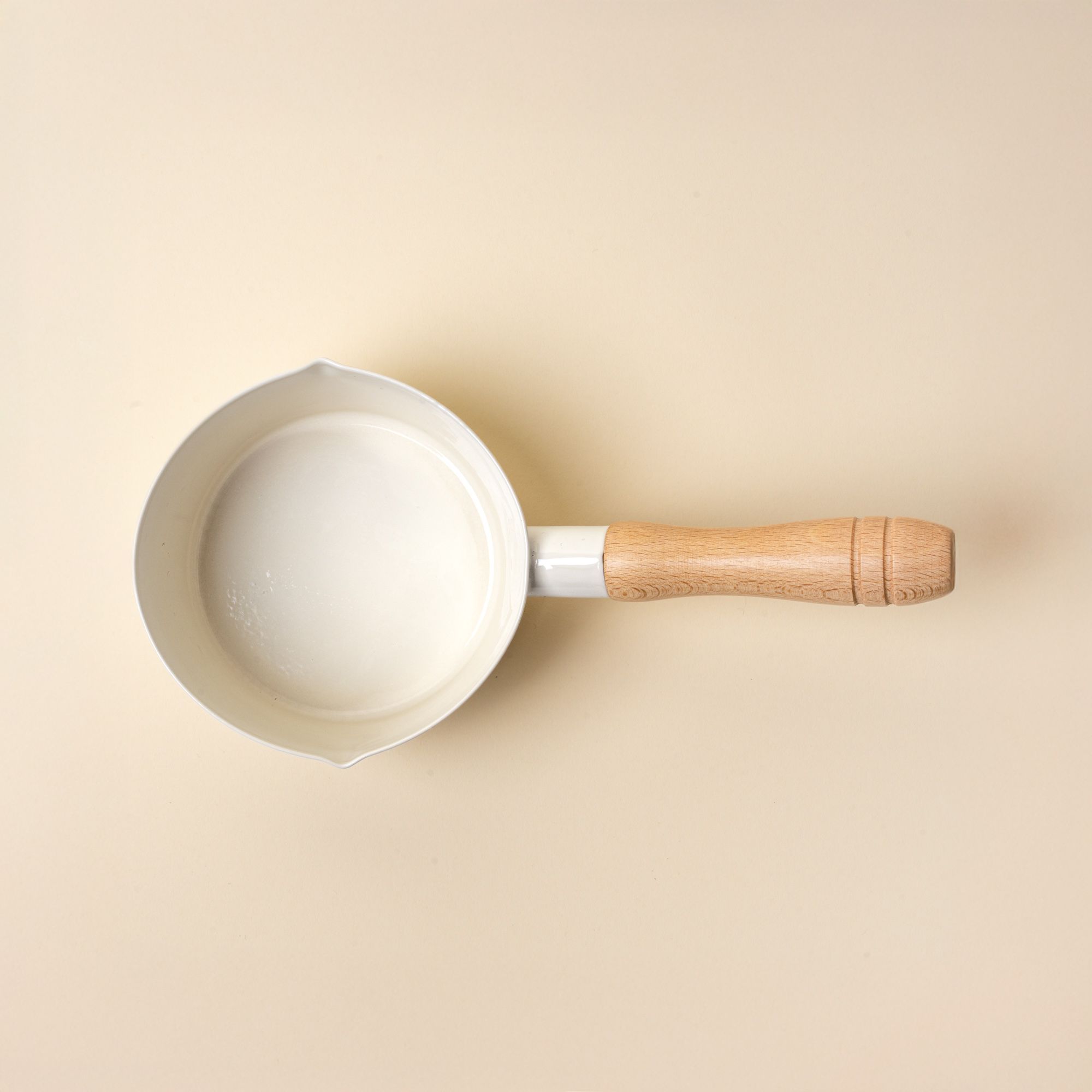An overhead view of a white enamel pot with simple spouts on the side with a wooden handle