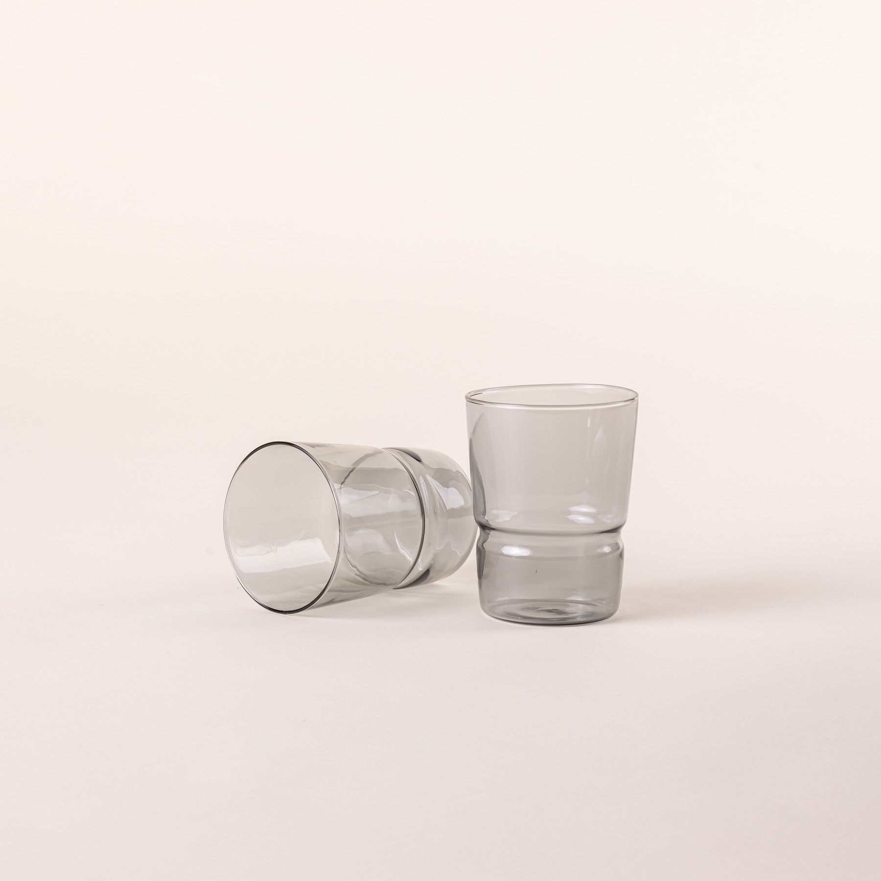 Two tumbler glasses that widens at the top in a grey color, 1 is standing up and 1 is laying on the side.