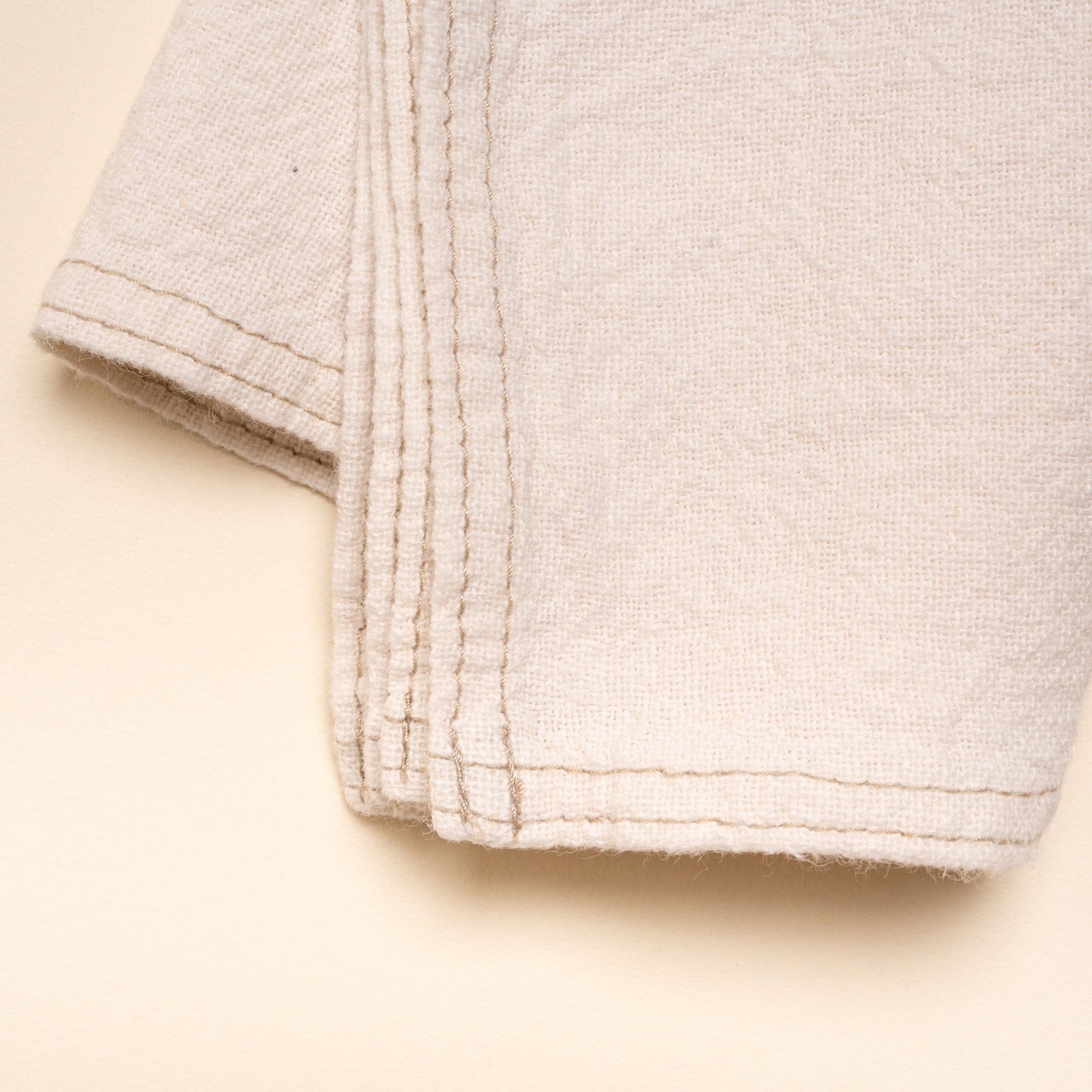 A closeup of the corner of a folded cream linen napkin with sewn edge