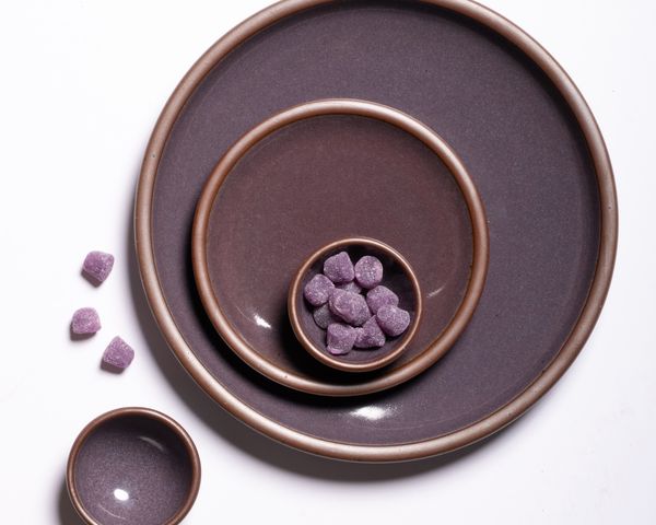 An overhead view of plates and small bowls artfully arranged in a purple color with soft glowing sheen and sprinkled gumdrops.